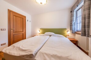 Un lit double avec une tête de lit verte, des lampes de chevet, une porte en bois et une fenêtre avec des rideaux.
