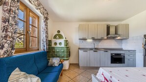 A compact living space with a sofa, a small table, a kitchen with cabinets and a stove, and a window with curtains.