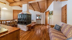 A cozy room with a wooden ceiling, a built-in stove, a sofa, and a dining table.