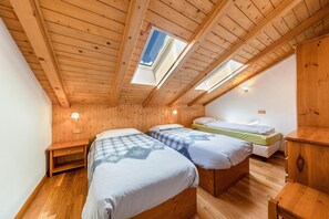 A room with wooden ceiling beams, two beds with checkered bedding, a small bedside table, and a wall-mounted light fixture.