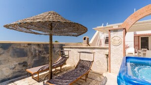 Une terrasse sur le toit, dotée de chaises longues, d’un jacuzzi et d’un mur en pierre.