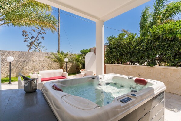 A hot tub with a stone wall backdrop, outdoor seating, and lush greenery.