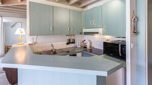 Una cocina moderna con gabinetes azul claro, un lavamanos de acero inoxidable, un microondas integrado y una isla grande con encimera de color claro.