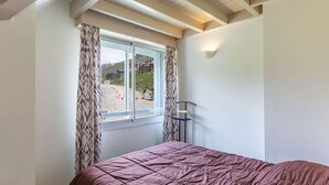 Un dormitorio con un ventanal grande, una cama con colcha morada y una lámpara de pared.