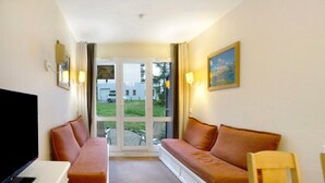 A hotel room with a sofa bed, a television, a painting, and a view of the outside. - Vacation Apartment "Ski-In/Ski-Out" Perfectly Located Year-Round (Valmeinier)