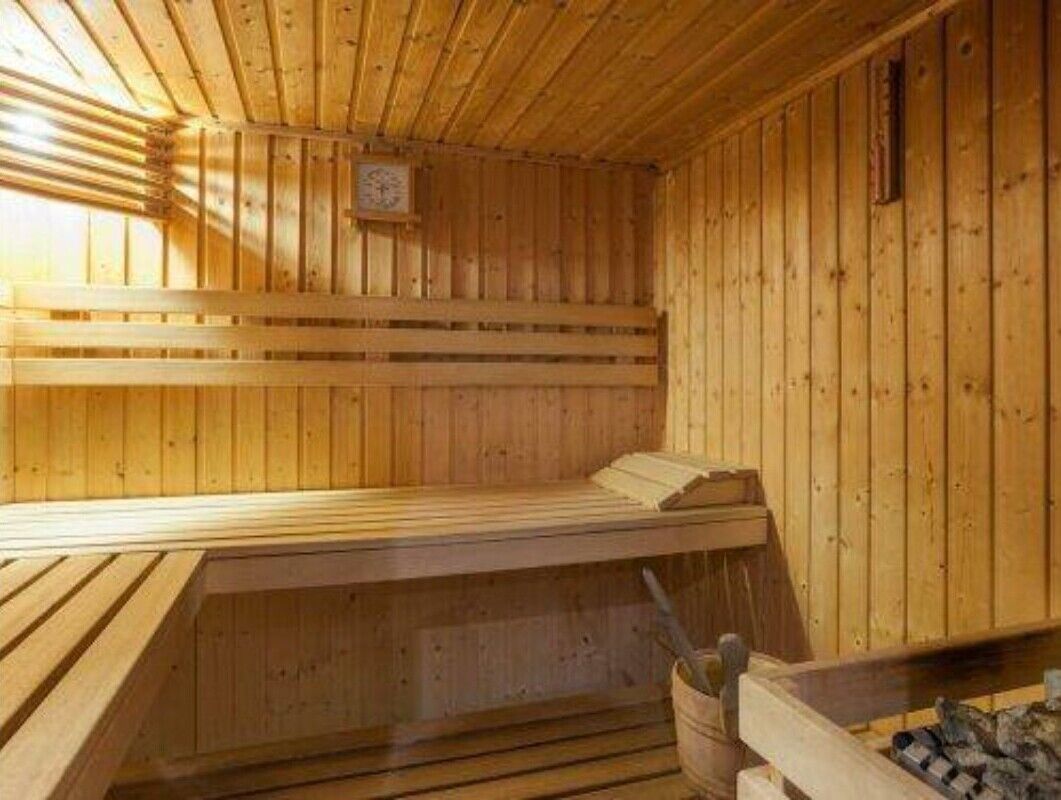 A wooden sauna with benches, a wooden ceiling, and a wall-mounted clock.