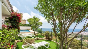 A poolside area with artificial grass, white lounge chairs, and a view of the sea.