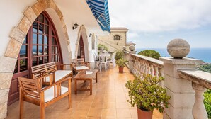 A terrace with stone arches, wooden furniture, and a view of the sea.