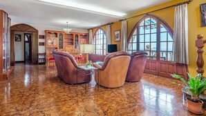A spacious lobby with a marble floor, leather armchairs, a chandelier, and large windows with curtains.