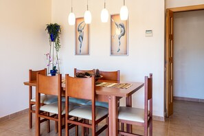 A dining area with a wooden table, chairs, hanging pendant lights, and two wall-mounted artworks.