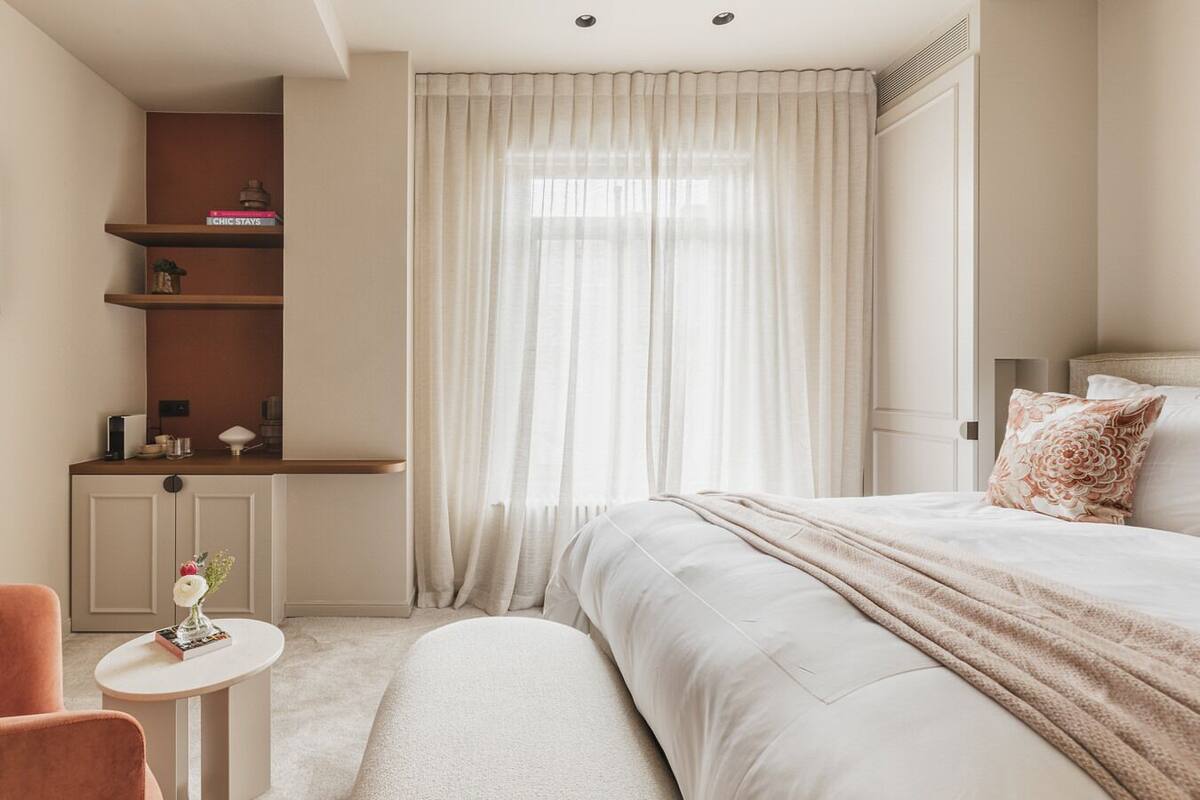 A modern bedroom with a large bed, a bedside table, a small round table, and a built-in shelf with books and decorative items.