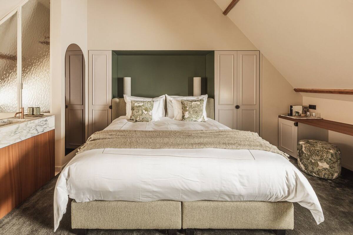 A bedroom with a large bed, a wooden bench, a small table, and a mirror.