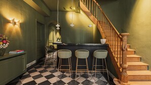 Uma área de bar com piso xadrez, escada de madeira e balcão com banquetas.