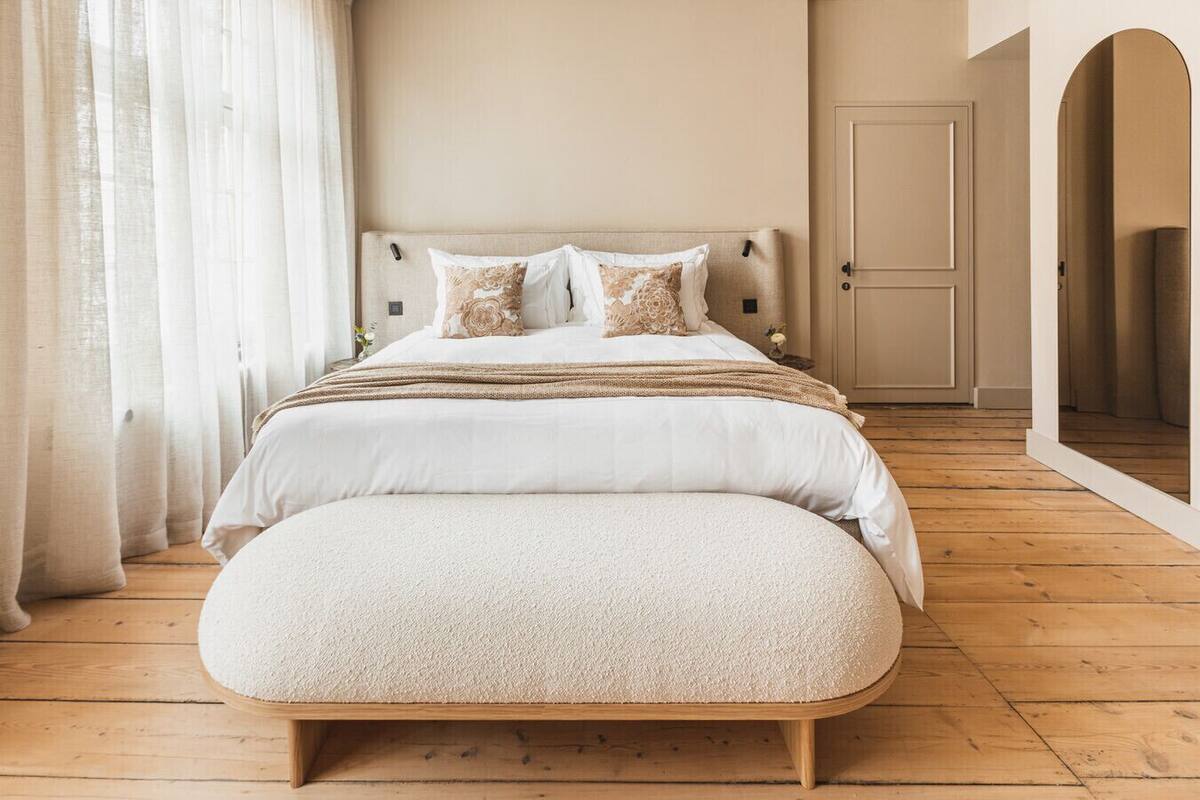 A bedroom with a bed, a wooden floor, a door, and a window with curtains.