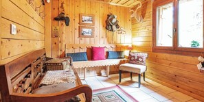 Interno di una baita in legno con una panca, un tavolino, una finestra vista e un appendiabiti a parete.