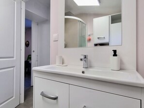 Ein modernes Badezimmer mit einem weißen Waschtisch, einem Spiegel und einer Duschkabine.