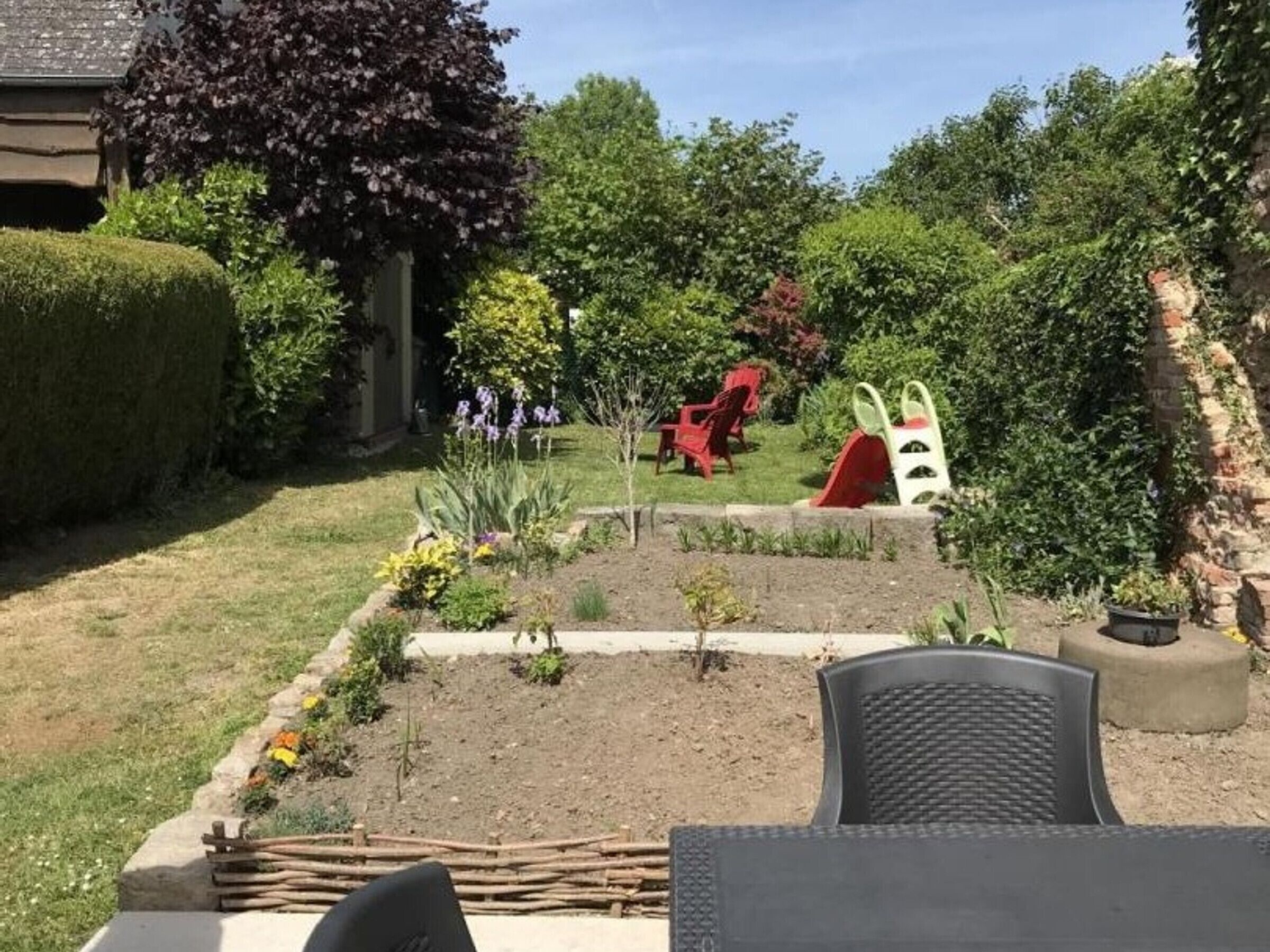 Un giardino con un'area giochi, che include uno scivolo e sedie rosse.