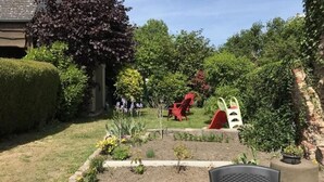 Ein Garten mit Spielbereich, darunter eine Rutsche und rote Stühle.