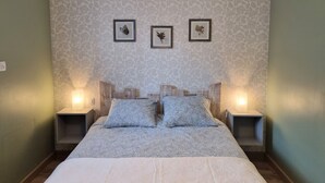 Ein Schlafzimmer mit gemustertem Tapetenbelag, einem Bett mit einer gemusterten Tagesdecke, zwei Nachttischen mit Lampen und drei gerahmten Bildern an der Wand.
