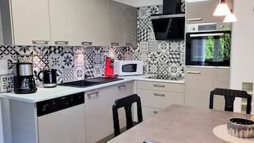 Een moderne keuken met een vaatwasser, koffiezetapparaat, magnetron en een eethoek met een tafel en stoelen.
