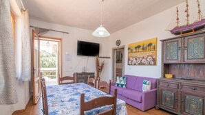 Een kamer met een bed, een paarse bank, een houten kast en een televisie aan de muur.