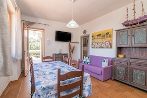 A room with a bed, a purple sofa, a wooden cabinet, and a television on the wall.