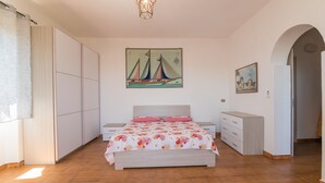 Een slaapkamer met een bed, een garderobe, een dressoir, een schilderij van een zeilboot en een schilderij van engelen.