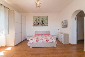 A bedroom with a bed, a wardrobe, a dresser, a painting of a sailboat, and a painting of angels.