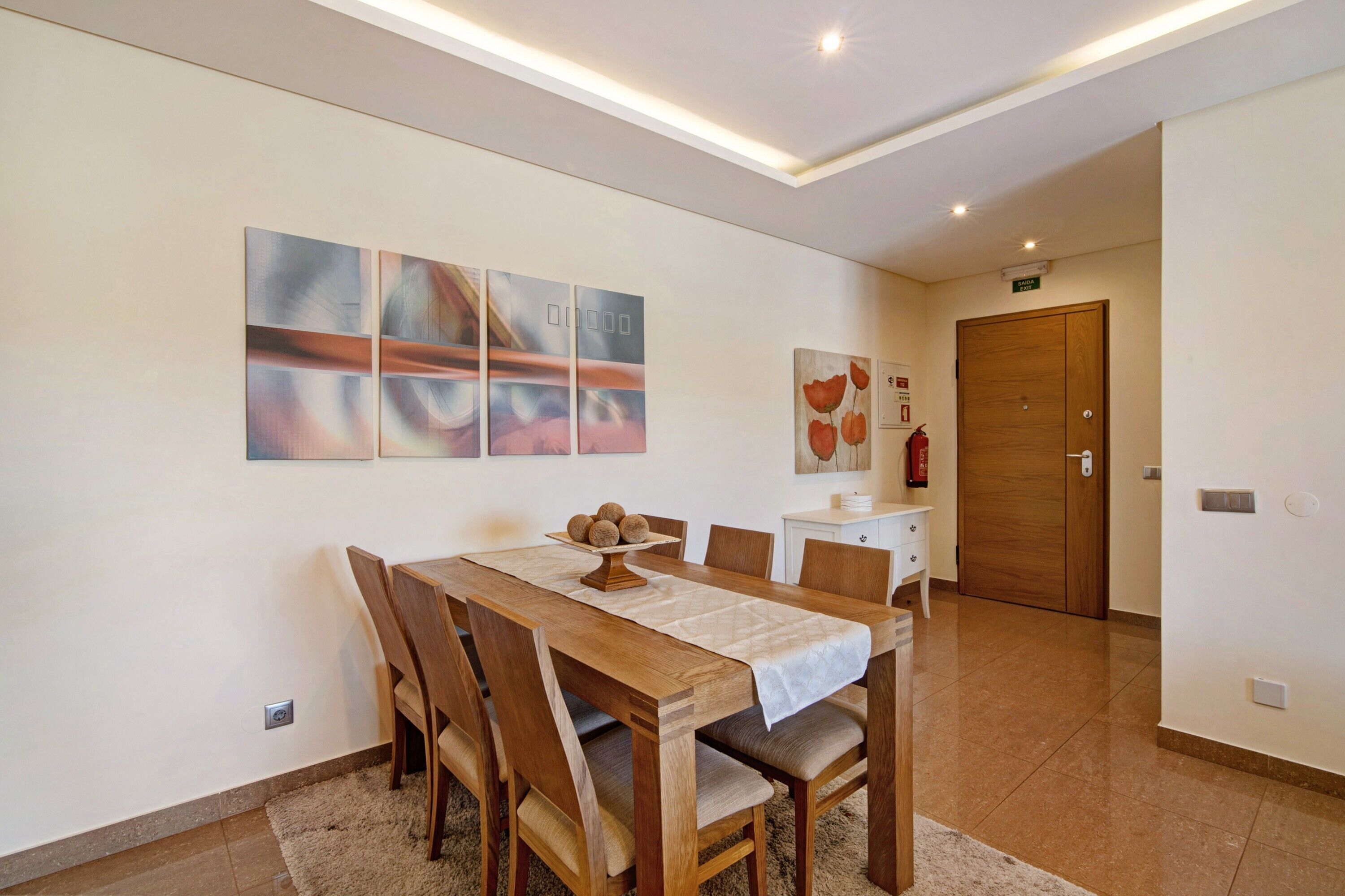 Un coin repas avec une table et des chaises en bois, une nappe blanche et une œuvre d’art accrochée au mur.