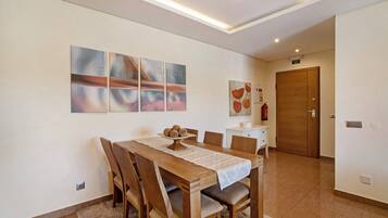 Un coin repas avec une table et des chaises en bois, une nappe blanche et une œuvre d’art accrochée au mur.