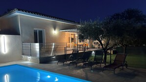 Une piscine avec des chaises longues, un patio couvert et une maison dotée d’un éclairage extérieur.