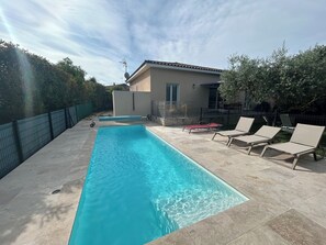 Piscina com espreguiçadeiras, um pequeno edifício e uma área cercada.