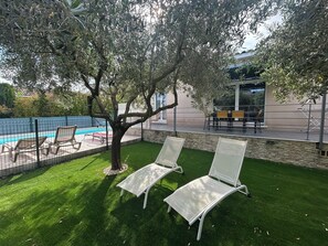 A poolside area with two lounge chairs, a tree, and a building in the background.