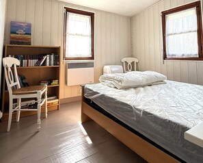 A bedroom with a bed, a chair, a bookshelf, and a window.