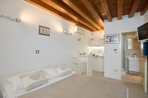 A bedroom with a bed, a desk, and a kitchenette.