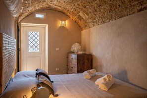 A bedroom with a stone arch, a bed with white linens, a wooden dresser, and a decorative wall piece.