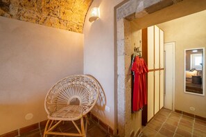A room with a wicker chair, a red garment on a rack, and a view of another room through an archway.