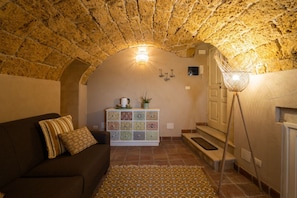 A cozy room with a stone ceiling, a patterned rug, a sofa with cushions, a cabinet with decorative tiles, and a floor lamp.