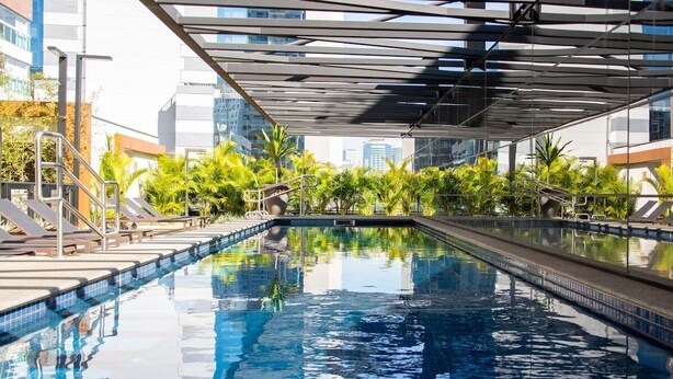 Une piscine dotée d’un toit en verre, entourée de palmiers et de chaises longues.