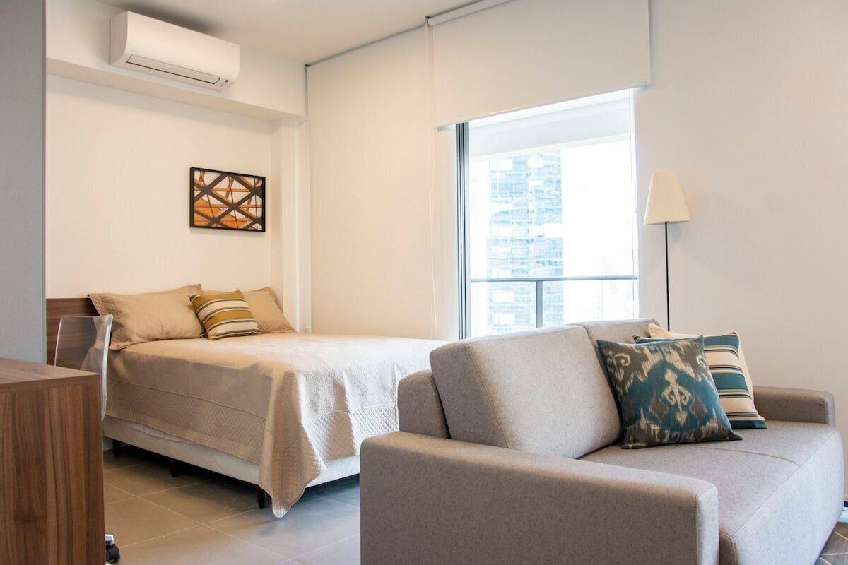 Une chambre d’hôtel moderne équipée d’un lit, d’un canapé, d’un bureau et d’une grande fenêtre donnant sur la ville.