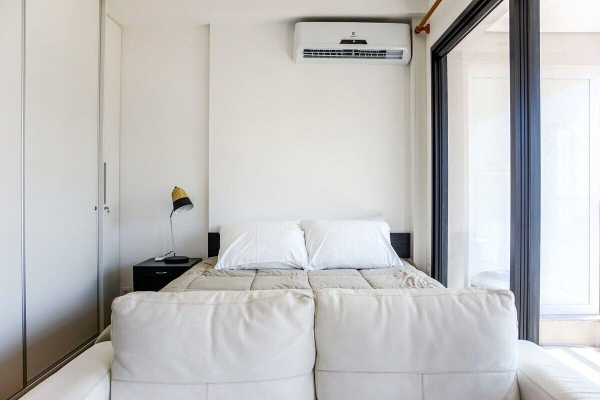 Une chambre à coucher comprenant un lit, une table de chevet, une lampe et un appareil de climatisation.