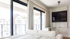 Une chambre avec un grand lit, un téléviseur fixé au mur et un balcon avec des rideaux.