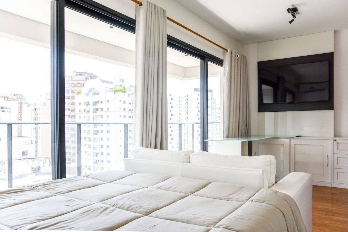 Une chambre avec un grand lit, un téléviseur fixé au mur et un balcon avec des rideaux.