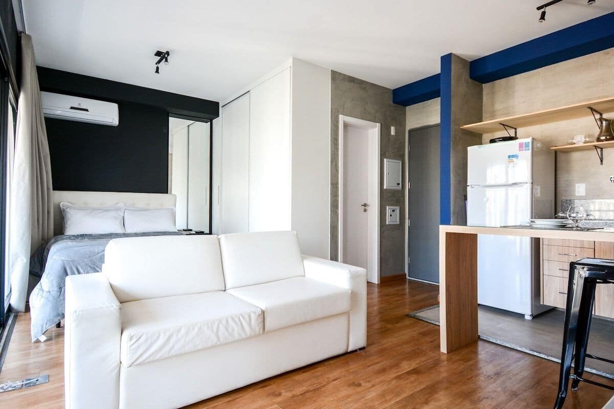 Une chambre d’hôtel moderne équipée d’un lit, d’un canapé blanc, d’une kitchenette et d’une salle de bain.