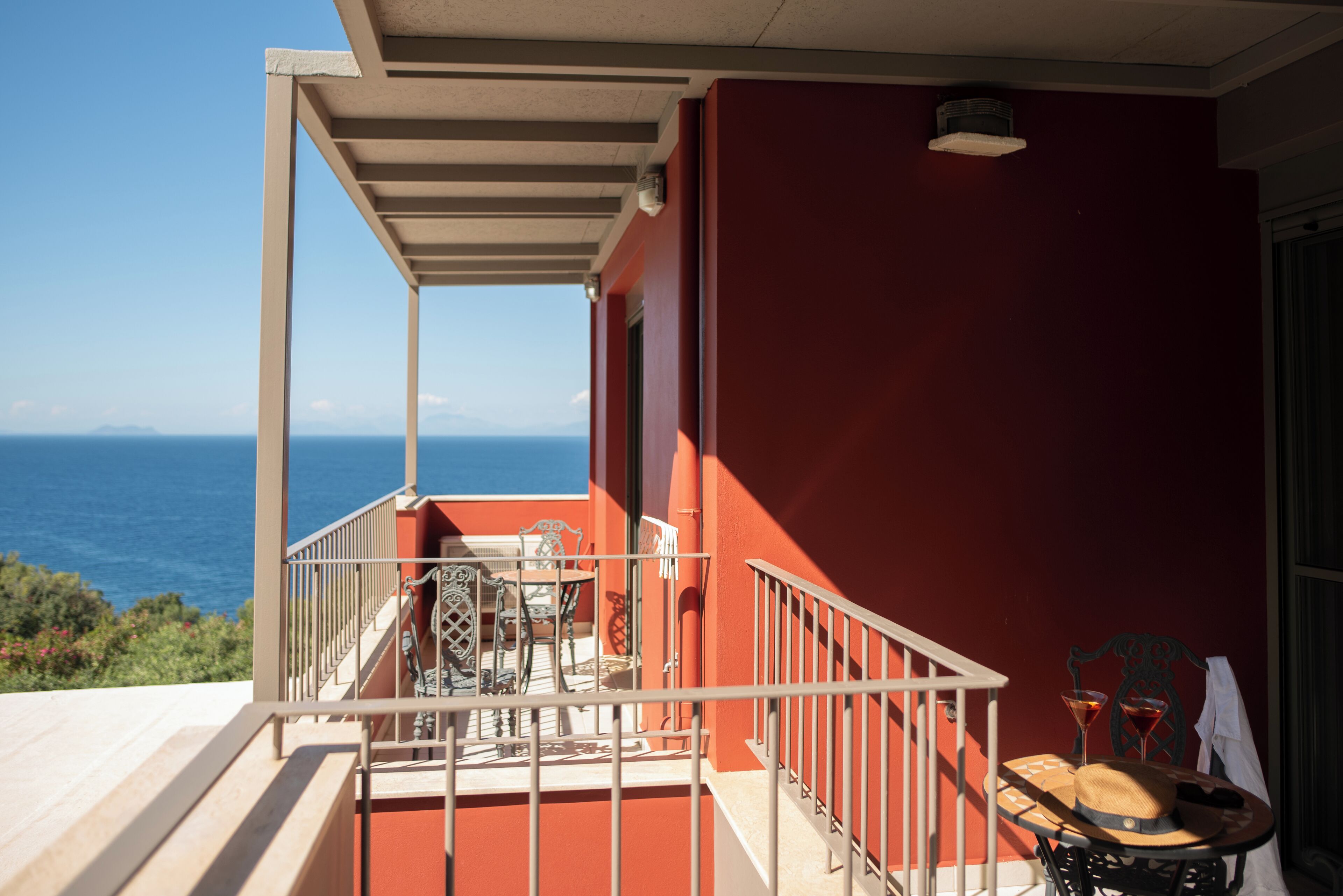 Un balcón con vista al mar, una mesa con sillas y una mesita con un sombrero y una bebida.