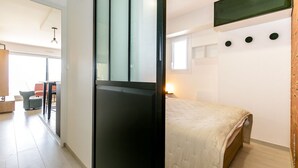A modern hotel room with a bed, a desk, and a chair. There is a window with blinds and a wall-mounted TV. - Super apartment with sea view (Quiberon)
