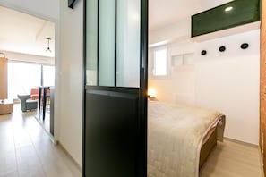 A modern hotel room with a bed, a desk, and a chair. There is a window with blinds and a wall-mounted TV. - Super apartment with sea view (Quiberon)