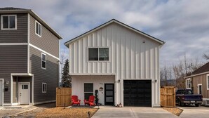 A two-story residential building with a garage, a front porch with red chairs, and a driveway.