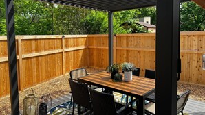 A covered outdoor patio with a wooden table and chairs, surrounded by a wooden fence and a wooden deck.