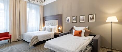 A hotel room with two beds, a red chair, a chandelier, and a floor lamp.